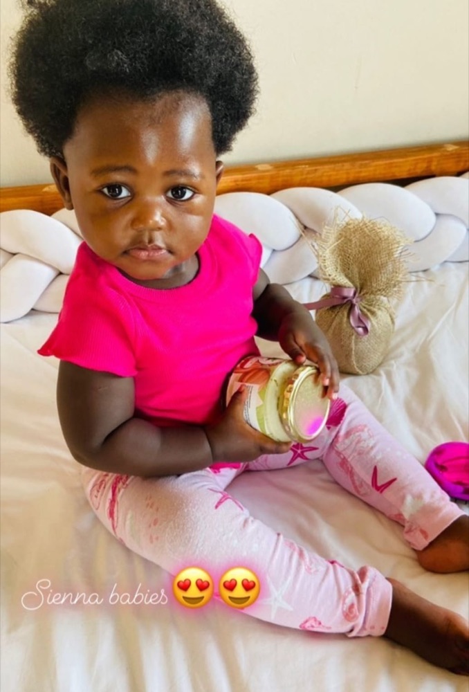 A young child holding a jar of Sienna Shea Butter